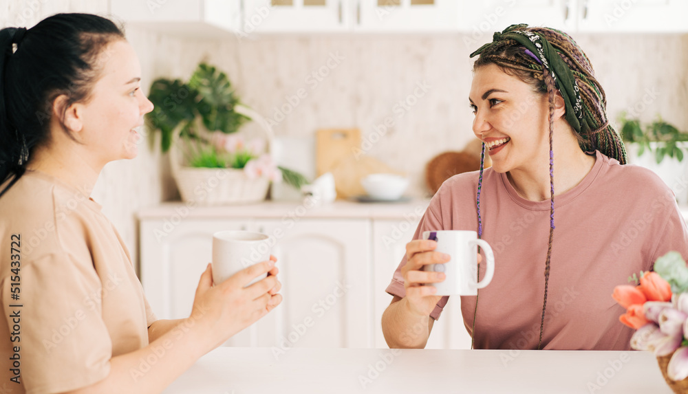 Two girls with mugs of coffee talking at the table.