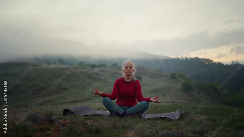 Senior woman doing breathing exercise in nature on early morning with fog and mountains in background. Senior woman doing breathing exercise in nature on early morning with fog and mountains in background.