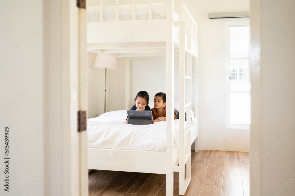 Asian little sibling watching video clip on tablet together in the bedroom with happy moment. Concept of technology, internet, social media, conncection, learning, education and homeschool for kid. Asian little sibling watching video clip on tablet together in the bedroom with happy moment. Concept of technology, internet, social media, conncection, learning, education and homeschool for kid.
