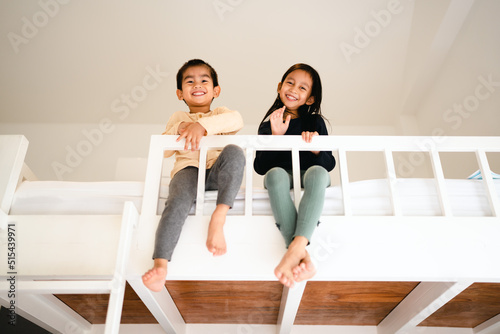 Asian little sibling are sitting on the bunk bed and looking to camera with big smile. Concept of love, relation, bonding friendship of brother and sister in family life.