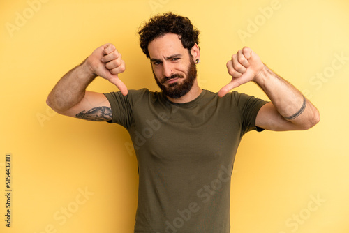 young adult bearded man looking sad, disappointed or angry, showing thumbs down in disagreement, feeling frustrated