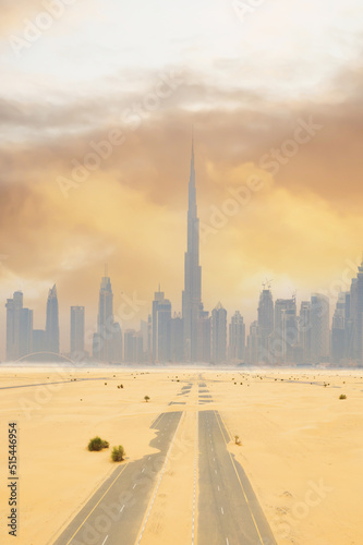 View from above, stunning aerial view of a deserted road covered by sand dunes with the Dubai Skyline in the distance during a beautiful sunset.