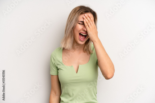 young adult blonde woman laughing and slapping forehead like saying d’oh! I forgot or that was a stupid mistake