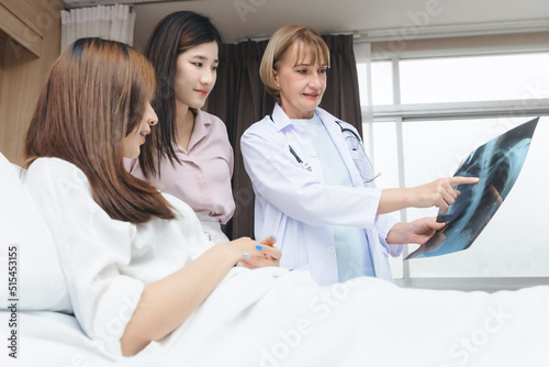 An expert doctor is explaining the X-ray results from the X-ray film to the patient and their relatives in the hospital room.