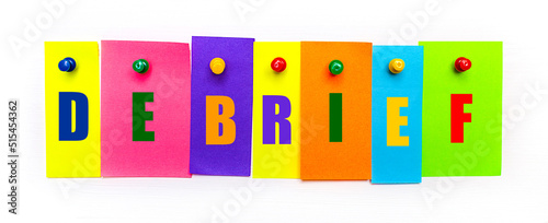 On a white background, buttons are used to fix bright multi-colored strips of paper with the text DEBRIEF