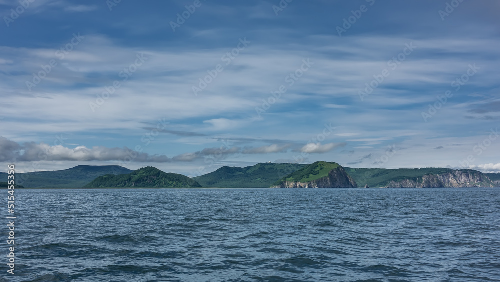 Picturesque hills and rocks are visible against the background of blue sky and clouds. Ripples on the surface of the Pacific Ocean. Kamchatka. Avacha Bay