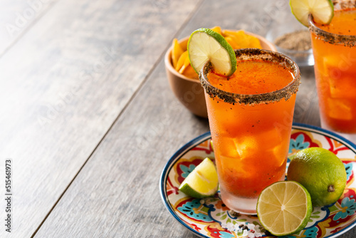 Homemade michelada cocktail with beer, lime juice,hot sauce,salted rim and tomato juice on wooden table. Copy space