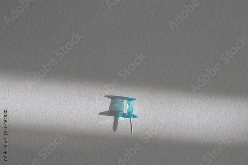 light blue push pin on a white paper in a beam of light