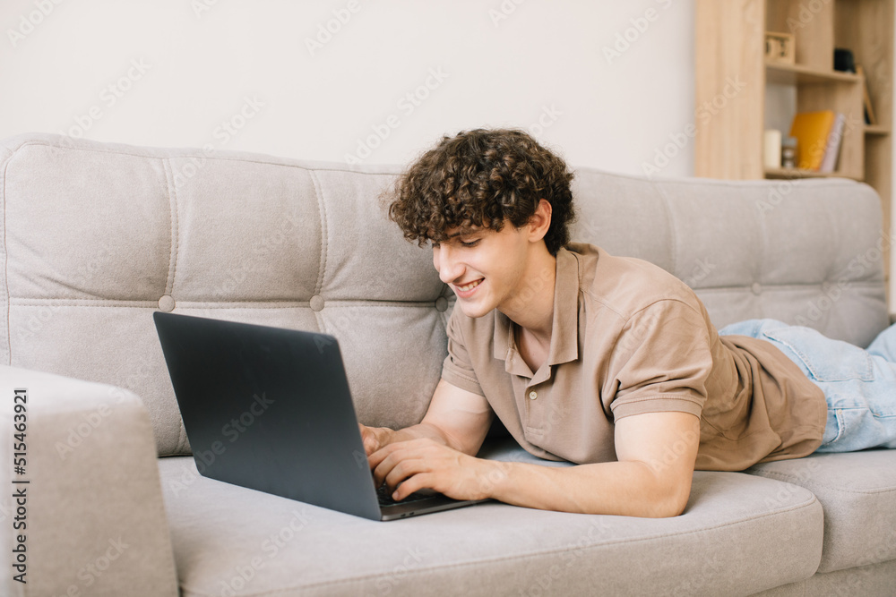 Portrait of attractive young curly hair man lying on the sofa and using laptop