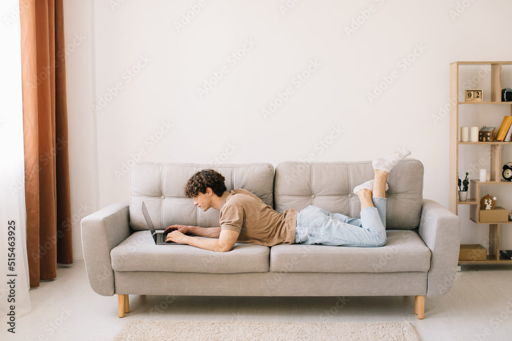 © anatoliycherkas - Portrait of attractive young curly hair man lying on the sofa and using laptop © anatoliycherkas - Portrait of attractive young curly hair man lying on the sofa and using laptop