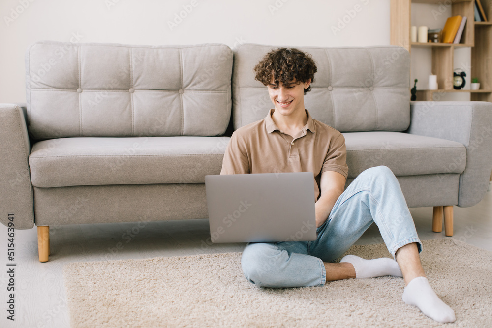 Portrait of attractive young curly hair man using laptop while sitting on sofa at home