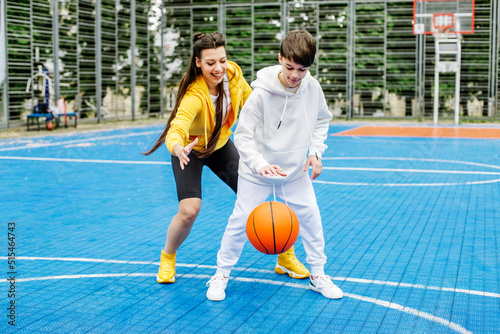 Girl and her younger brother, teenager, play basketball on modern basketball court under open sky © Olha Tsiplyar