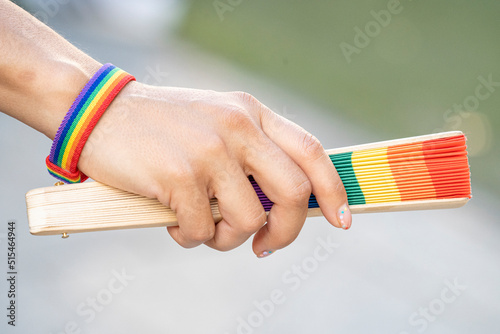 Woman holding a fan with the multicolored gay flag, a rainbow bracelet and multi-colored fingernails, on the occasion of gay and LGBTI pride during a sunny summer day