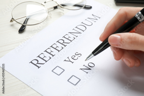 Woman with referendum ballot making decision at white table, closeup photo