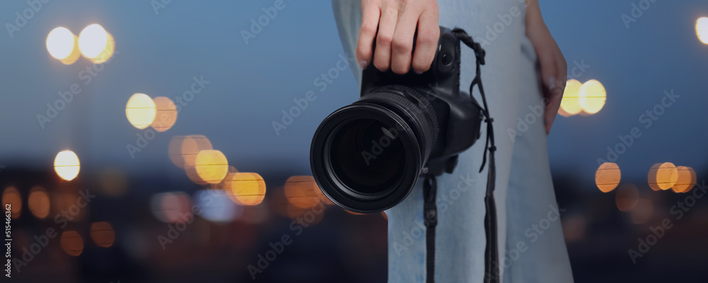 Professional photographer with modern camera and blurred view of beautiful city in evening. Banner design - obrazy, fototapety, plakaty 