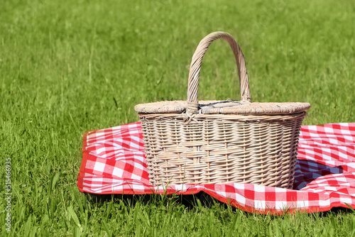 Picnic basket with checkered tablecloth on green grass outdoors, space for text