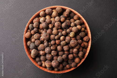 Bowl of allspice pepper grains on grey background, top view photo