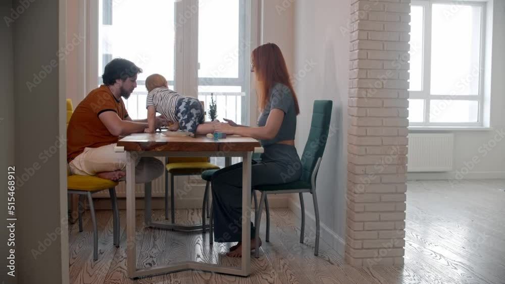Stressful man trying to work with his laptop while his baby crawls on the table - his wife takes away the baby and walks in other room Stressful man trying to work with his laptop while his baby crawls on the table - his wife takes away the baby and walks in other room