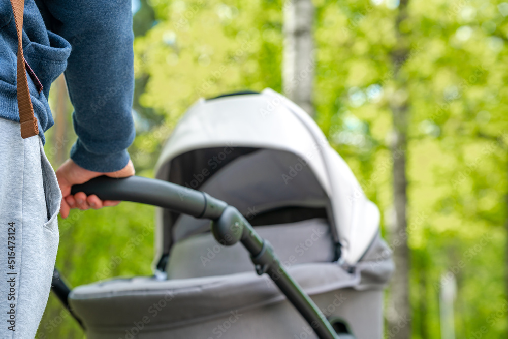 A man is driving a baby carriage. A young father walks with a newborn baby in a stroller on a summer day A man is driving a baby carriage. A young father walks with a newborn baby in a stroller on a summer day