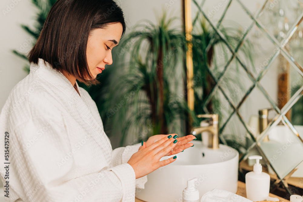 Facial Skincare. Happy Korean asian woman applying Facial serum using dropper standing in modern bathroom. Female moisturizing caring for skin using natural oil looking at the bottle Facial Skincare. Happy Korean asian woman applying Facial serum using dropper standing in modern bathroom. Female moisturizing caring for skin using natural oil looking at the bottle