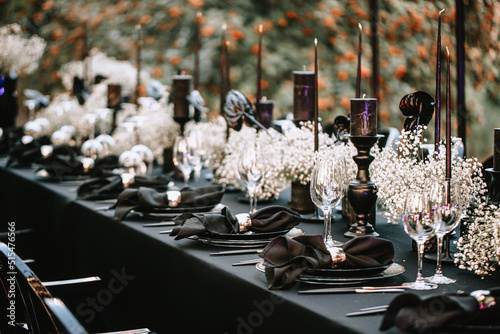 Serving and decorating a banquet table in black with white flowers and black candles at an outdoor party. photo