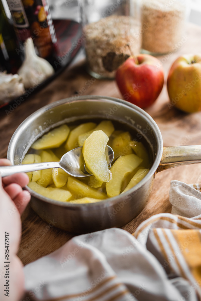 compote of fresh apples in a metal pot in the kitchen. a piece of apple loaded on a fork held in the hand (selective focus, blurred background)