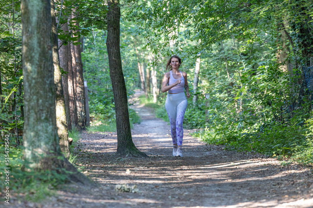 Blonde Caucasian young fitness woman running on forest trail in the sun. Exercising outdoors is healthy for active lifestyle runners. Autumn trail run woman running in nature, Outdoor jog. High