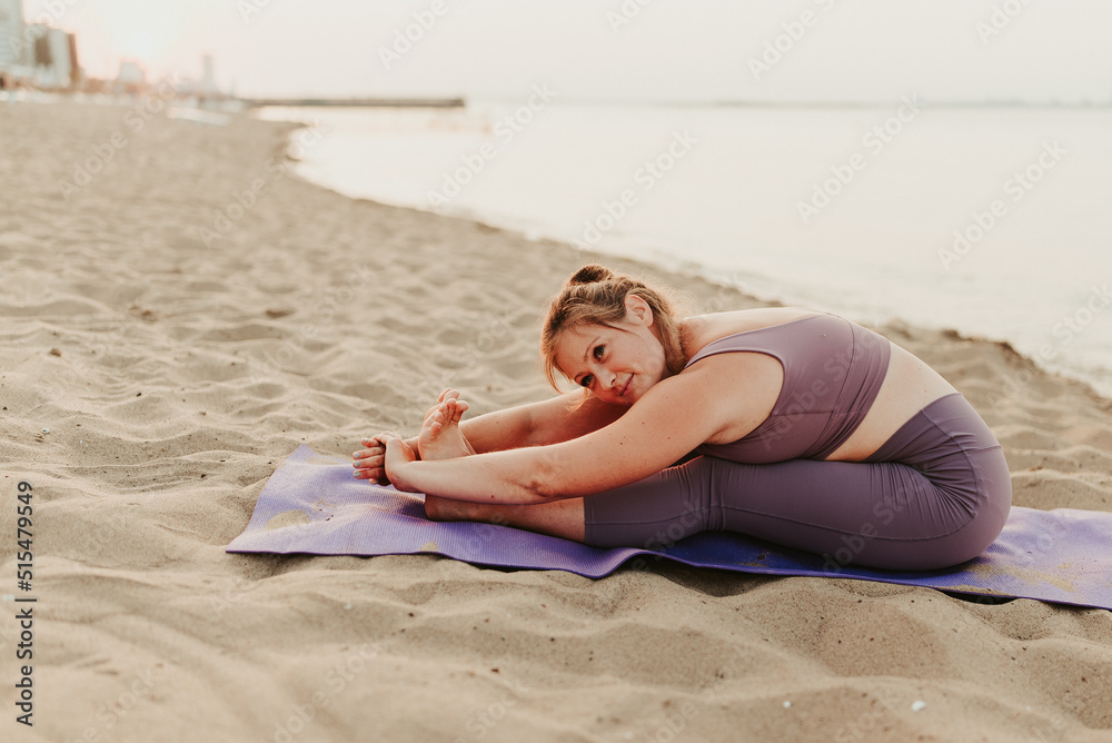 Caucasian woman practicing yoga at seashore sandy beach on sunrise. Womens health and wellness. Sports body positive