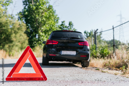 Broken down black car accompanied by an emergency warning triangle. Vehicle parked on the shoulder marked as broken down.