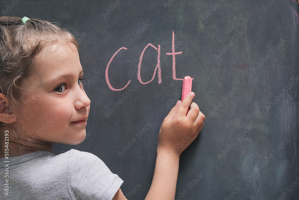 blonde girl writes the word cat in chalk on the chalkboard