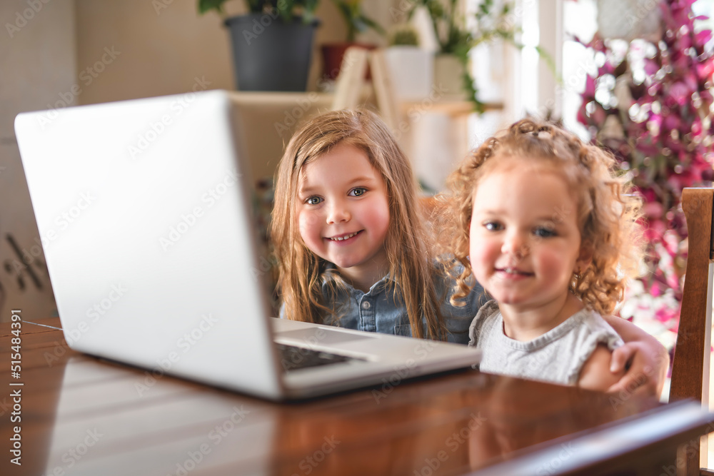 Two girls using laptop on the kitchen table Two girls using laptop on the kitchen table