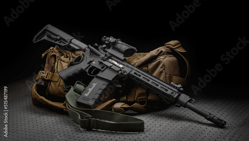 A modern automatic carbine with a collimator sight. The weapon lies on a military backpack. Rifle for the police, special forces or the army. Dark back.