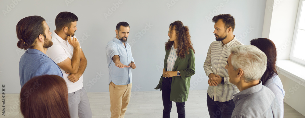 Obraz premium Group of serious people standing and talking. Modern coach meeting with business team, teaching, helping, sharing expert guidance, explaining how to find better solution and work out success strategy