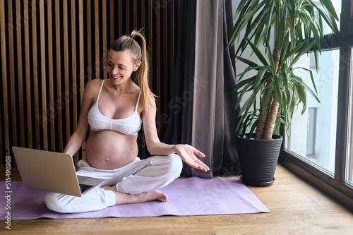 beautiful pregnant business woman in glasses sitting on the floor on a mat using a laptop and notebook working at home