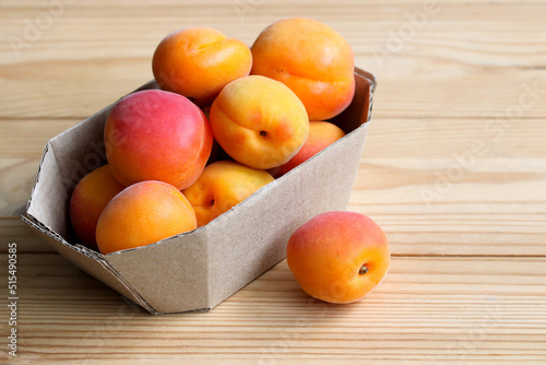 ripe apricots in a cardboard tray on a wooden background.