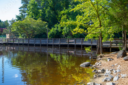 a gorgeous summer landscape in the park with a brown wooden bridge over a lake surrounded by rocks and lush green trees, grass and plants with blue sky and clouds at Dupree Park in Woodstock Georgia photo