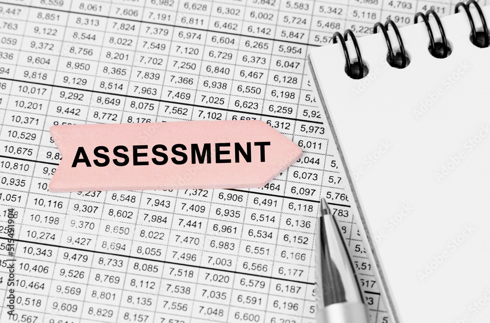 Fototapeta premium On the table among the reports is a notebook, a pen with an arrow with the inscription - ASSESSMENT