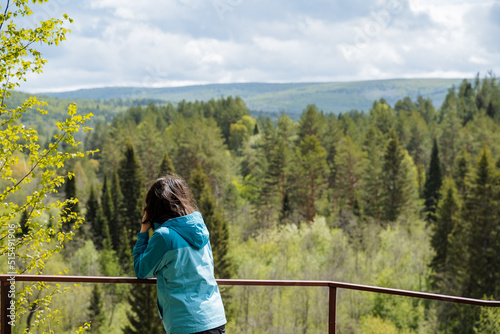 A girl in a jacket stands on the observation deck admiring the beautiful view of the mountains, the view from the back of a woman in the forest, hiking.
