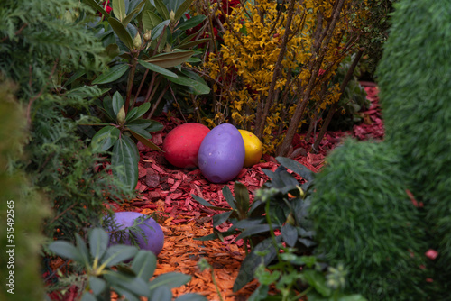 Colorful Easter eggs lies on the ground by green bushes and blooming flowers. Selective focus. Easter holiday decortions theme. photo