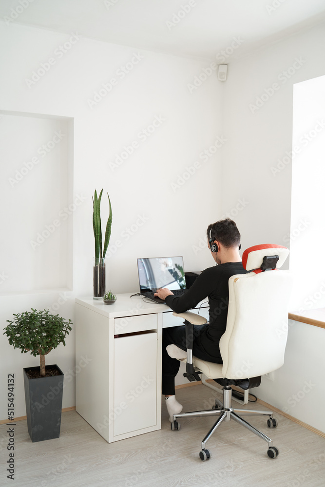 Guy in headphones working on laptop in light interior Guy in headphones working on laptop in light interior
