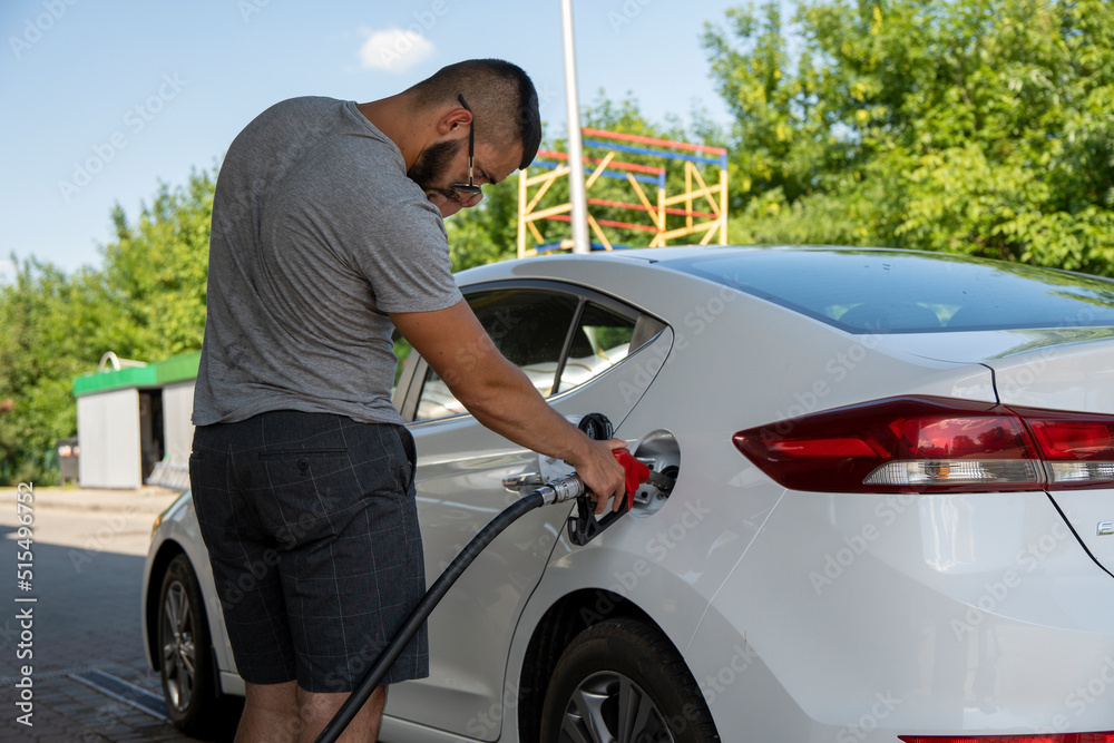 A young man pours gasoline into the gas tank of a white car.A young man pumps gasoline into a gas tank. Fuel and oil crisis. The concept of gasoline prices and the oil crisis.