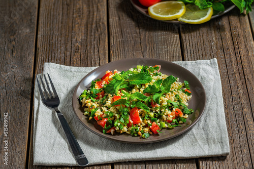 on a wooden brown background in a plate appetizing vegetarian oriental salad tabbouleh with boiled bulgur and tomatoes, seasoned with lemon juice and olive oil with herbs
