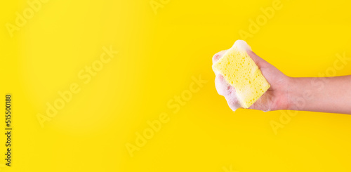 Persons hand holding yellow sponge for dish wash. Washcloth covered in soap. Domestic chores and supplies concept. Sensitive dishwashing detergent. Copy space in left side. Isolated on yellow
