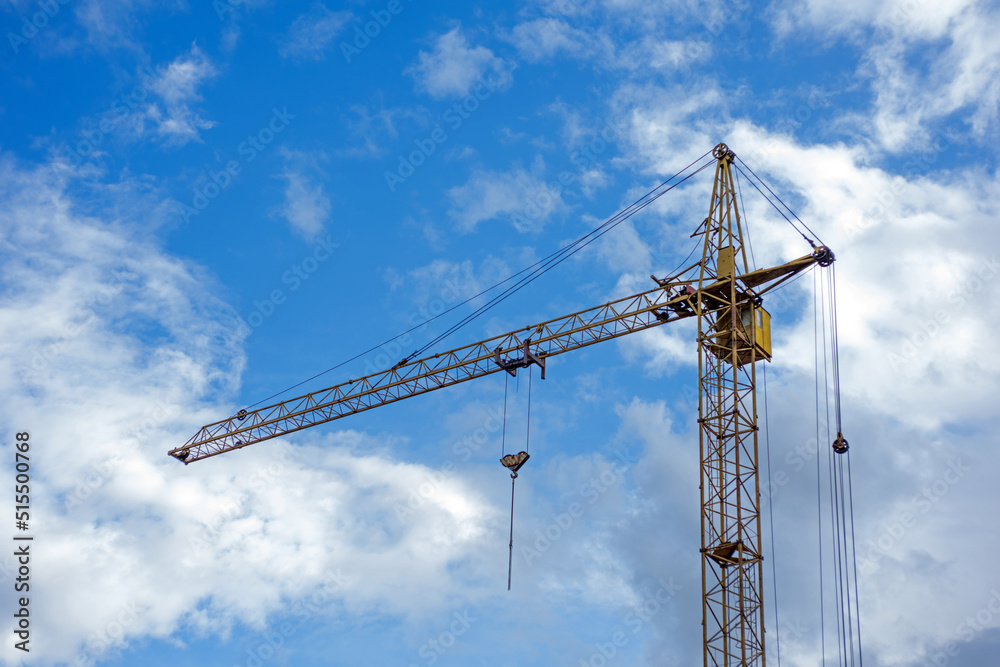 Metal yellow construction crane against a blue sky with clouds, building