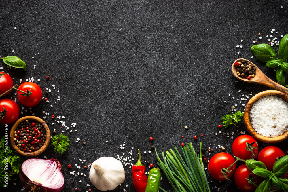 Food background on black stone table. Fresh vegetables, herbs and spices. Ingredients for cooking with copy space.