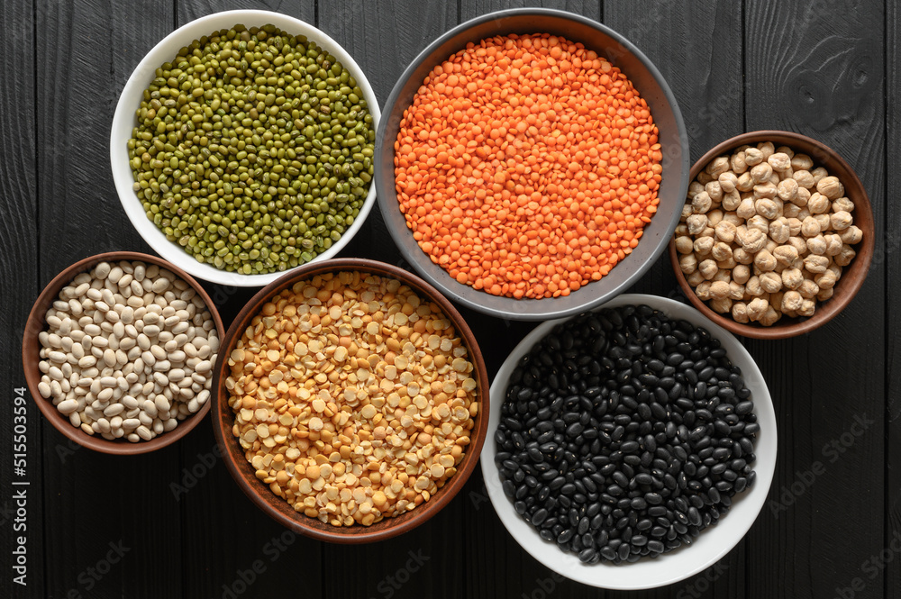 Overhead view of bowls of assorted raw legumes on a dark wooden table Overhead view of bowls of assorted raw legumes on a dark wooden table