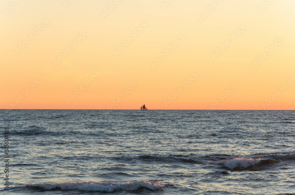 A ship sailing along the horizon during sunset