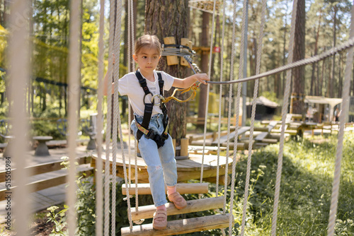 Beautiful little child climbing and having fun in adventure park. Children summer activities. Child climbing on rope park. 