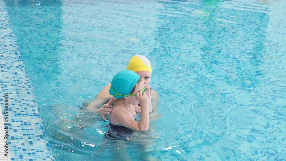 Little girl learning to swim with mother in big sport pool. Swimming school for small children. Healthy kid enjoying active lifestyle. Preschooler practicing with foam pad and noodle.
