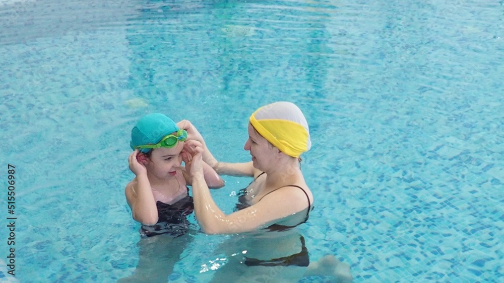 Little girl learning to swim with mother in big sport pool. Swimming school for small children. Healthy kid enjoying active lifestyle. Preschooler practicing with foam pad and noodle.
